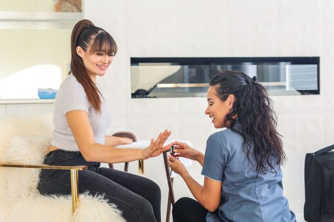 Smiling woman receiving a professional manicure as a nail technician applies polish in a bright, modern nail salon with a cozy chair.