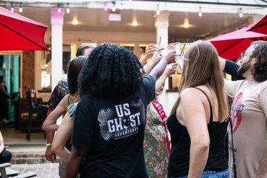 Friends raising drinks in a cheers on a lively outdoor patio with red umbrellas, casual summer outfits and a festive evening vibe.