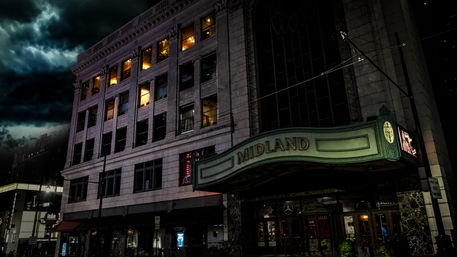 Moody night shot of a historic downtown theater with a curved illuminated marquee, ornate stone facade, and lit upper-floor windows under stormy clouds
