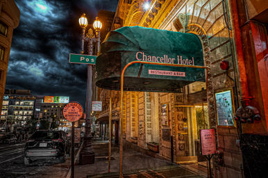 Downtown hotel entrance at night with a green canopy labeled 'Restaurant & Bar', ornate golden facade and vintage street lamps under a dramatic stormy sky, parked cars and city street scene.