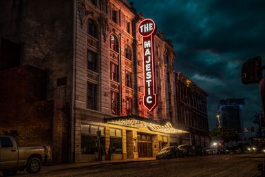 Historic downtown theater with tall vertical neon marquee and glowing canopy, ornate stone façade and parked cars on a moody nighttime city street