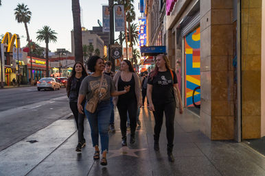 Group of people strolling down Hollywood Boulevard at dusk on the star-lined Walk of Fame, palm trees and neon theater signs glowing