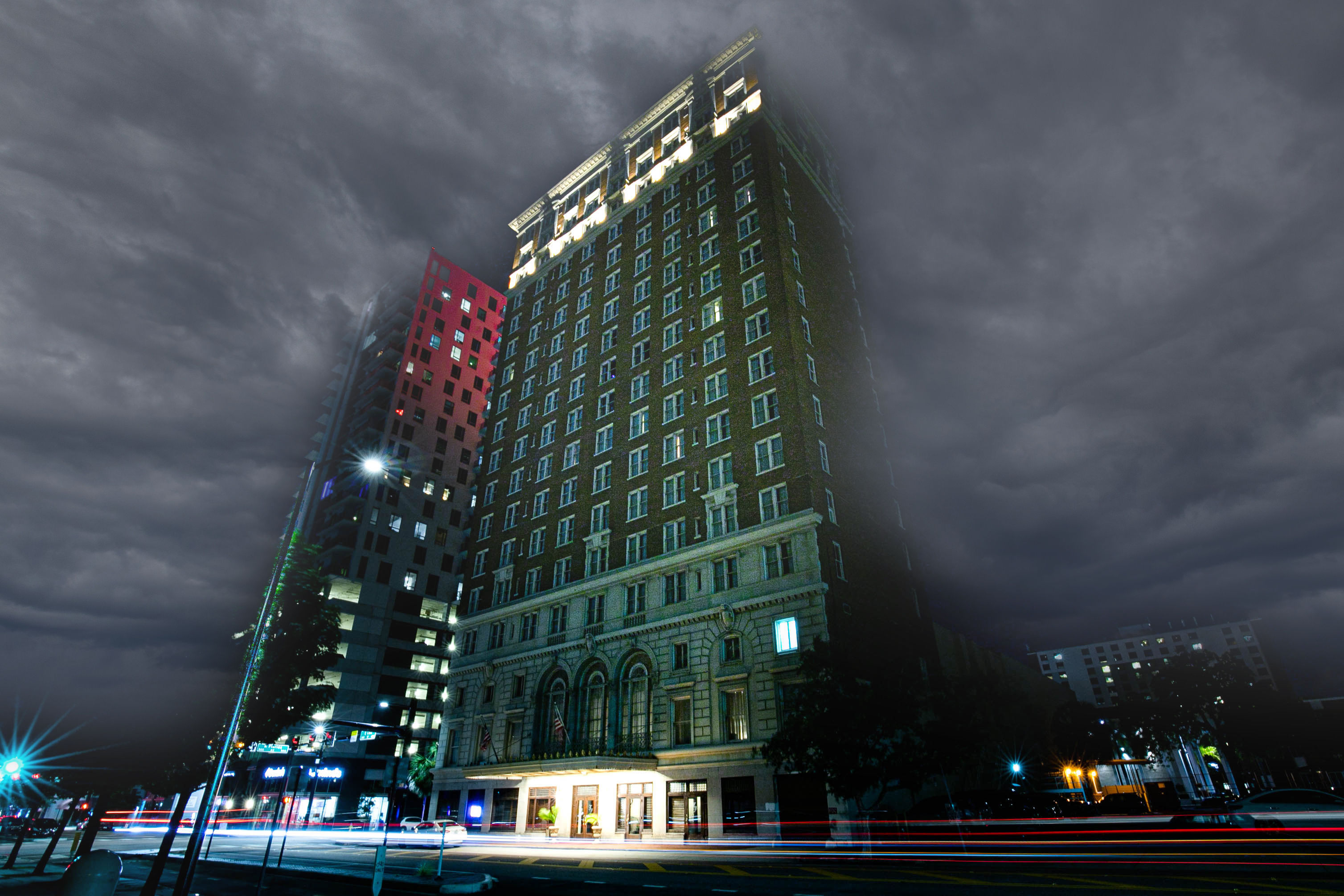 Historic brick high-rise hotel on a downtown street at night under dramatic storm clouds, with colorful car light trails and urban architecture.