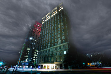 Historic brick high-rise hotel on a downtown street at night under dramatic storm clouds, with colorful car light trails and urban architecture.
