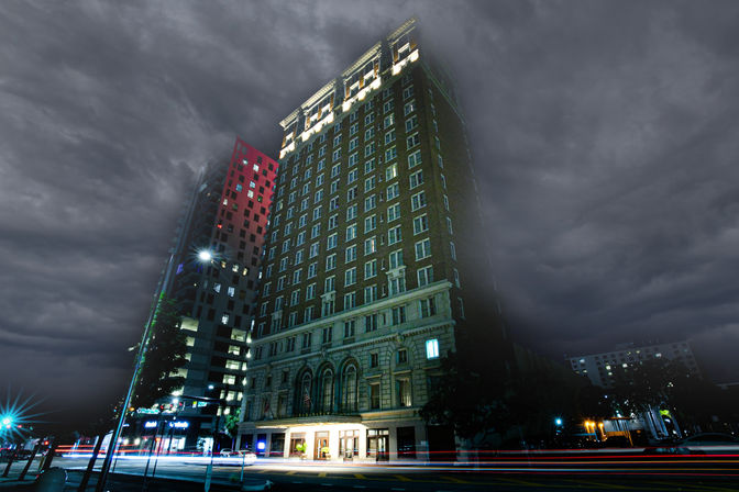 Historic brick high-rise hotel on a downtown street at night under dramatic storm clouds, with colorful car light trails and urban architecture.