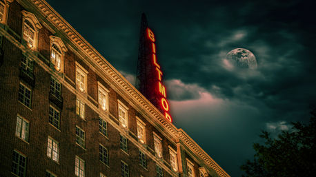 Cinematic moonlit historic brick hotel facade with a glowing vertical neon sign against a moody, cloudy night sky.