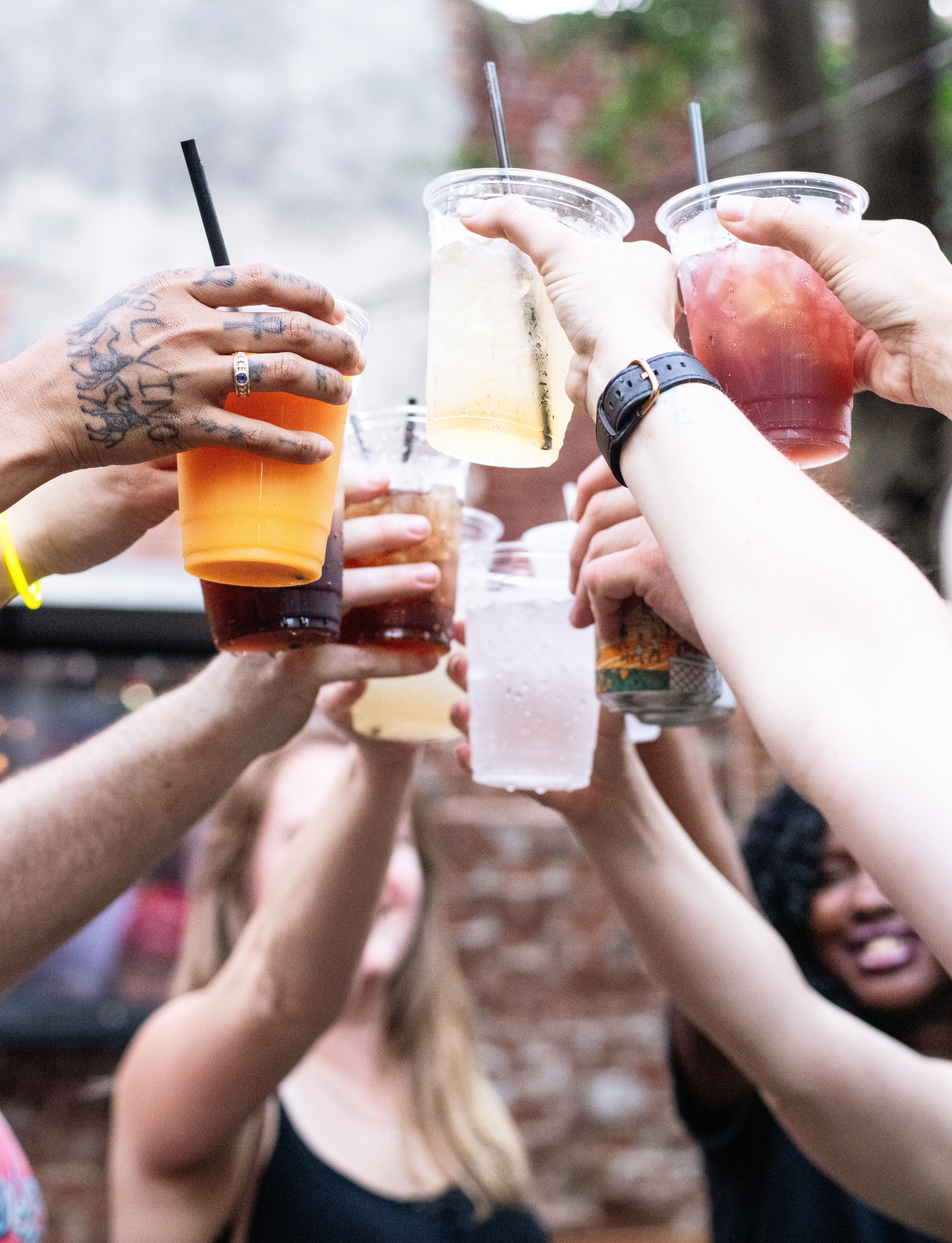 Group of hands raising plastic cups of colorful iced drinks for a cheerful outdoor patio toast