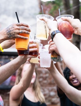 Group of hands raising plastic cups of colorful iced drinks for a cheerful outdoor patio toast