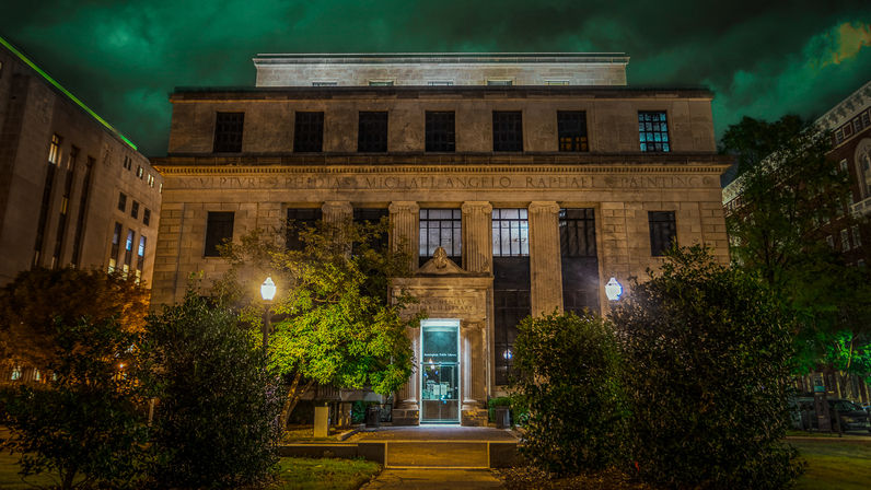 Moody nighttime scene of a historic neoclassical stone building with tall columns and a glowing entrance, flanked by trees and lampposts under a green-tinted sky
