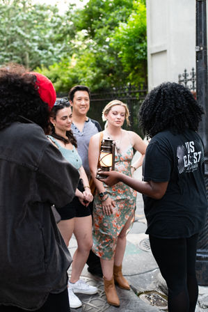 Small group on a city walking tour listening to a guide holding a glowing lantern on a tree-lined urban sidewalk