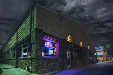 Nighttime urban corner bar in a brick building with a glowing neon OPEN sign in the window, warm exterior lamps, empty sidewalk and moody storm clouds overhead.