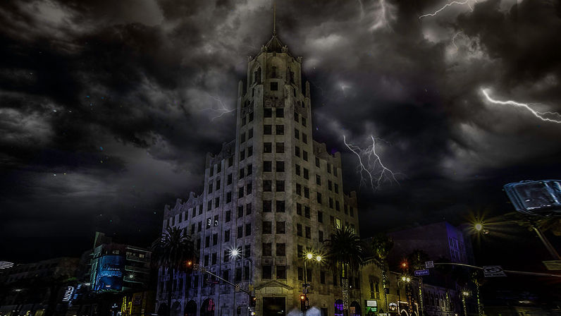 Historic downtown stone tower and palm-lined city street at night, lit street lamps and neon with dramatic lightning bolts and dark storm clouds overhead.