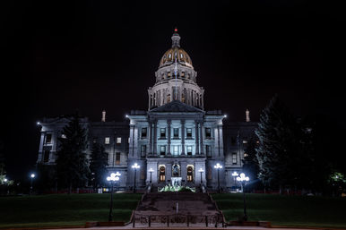 Night view of an illuminated neoclassical capitol building with a glowing gold dome, grand steps and vintage lamp posts against a dark sky