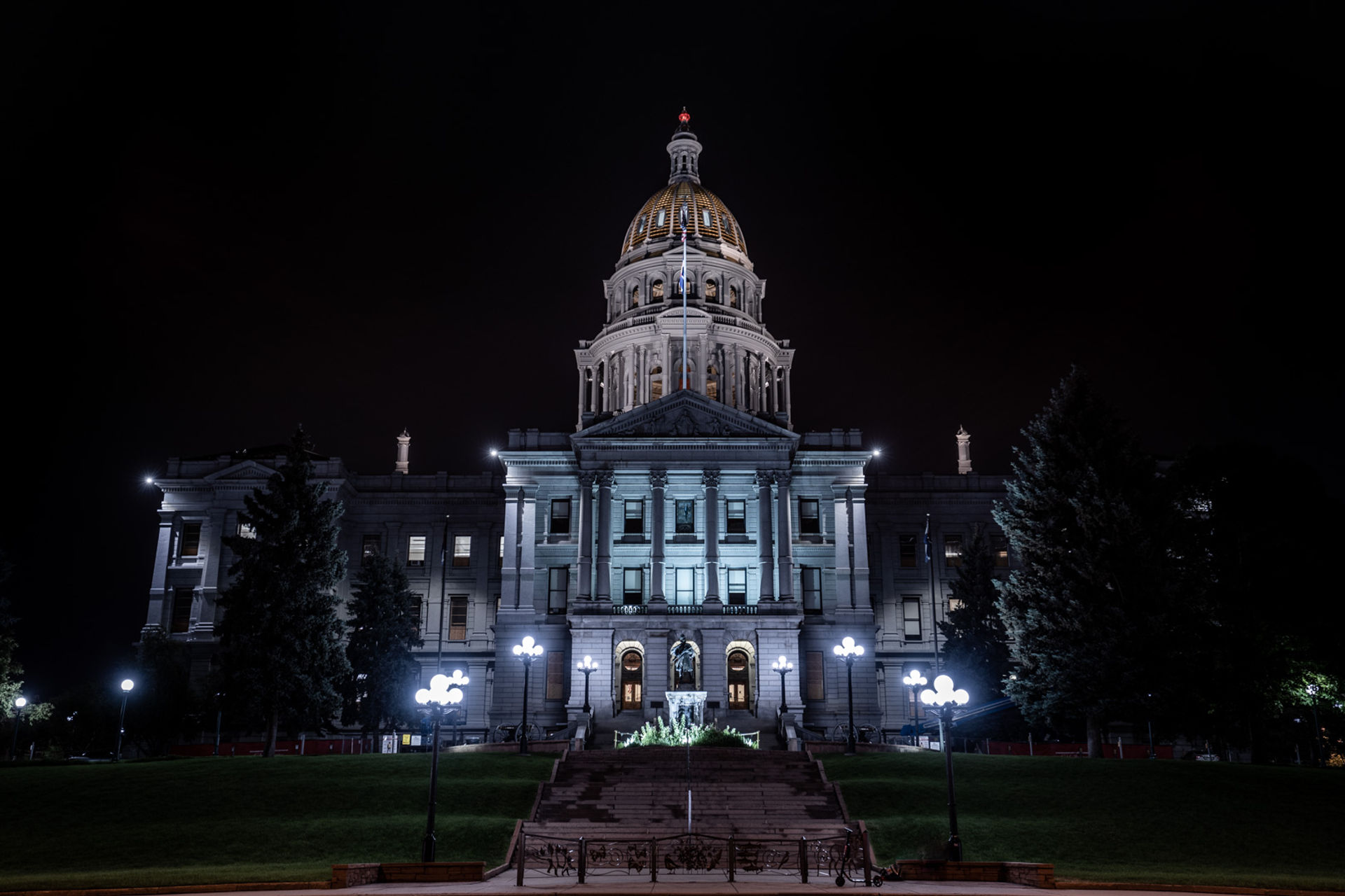 Night view of an illuminated neoclassical capitol building with a glowing gold dome, grand steps and vintage lamp posts against a dark sky