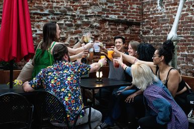 Group of friends toasting colorful cocktails at an urban brick-walled outdoor patio bar, lively evening vibe