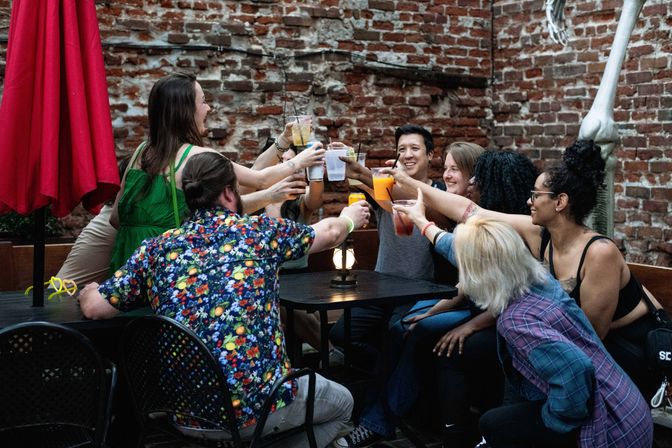 Group of friends toasting colorful cocktails at an urban brick-walled outdoor patio bar, lively evening vibe