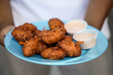 Blue plate of golden fried hush puppies (corn fritters) with two creamy dipping sauces, handheld appetizer close-up