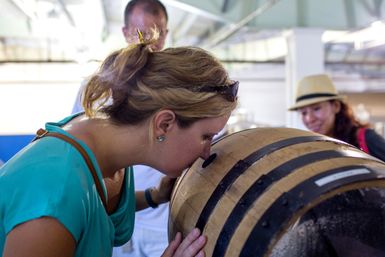 Visitor sniffing an oak barrel at a distillery tasting room — leaning in to inhale barrel-aged aromas while other guests watch.