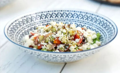 Bright Mediterranean cucumber and cherry tomato salad with crumbled feta and red onion in a blue patterned bowl on a white wooden table