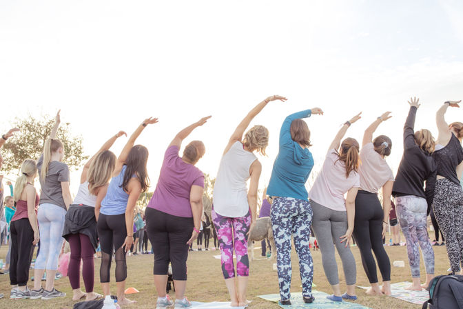 Women in colorful leggings performing side-bend stretches in an outdoor community yoga class on a grassy park at sunrise