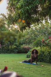 Woman practicing outdoor yoga in upward-facing dog on a blue mat on a green lawn in a lush tropical garden under an overhanging fruit tree at golden hour