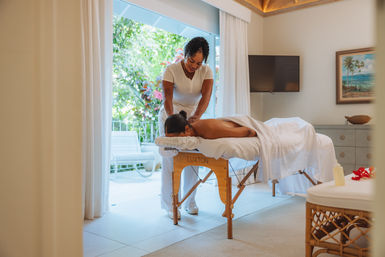 Relaxing tropical spa massage: therapist giving a back massage to a client on a treatment table in a bright room opening to lush garden