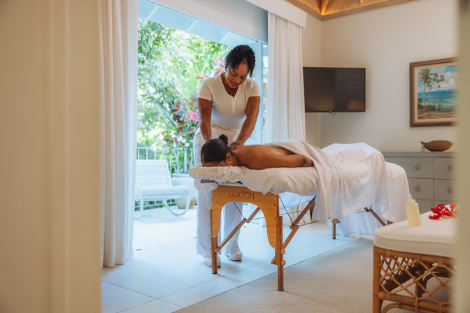 Relaxing tropical spa massage: therapist giving a back massage to a client on a treatment table in a bright room opening to lush garden
