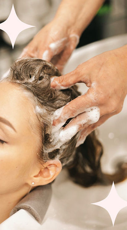 Bubbly salon shampoo: close-up of a woman reclined at a salon sink while a stylist lathers and massages her hair for a relaxing scalp treatment.