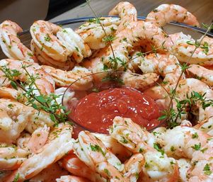 Shrimp cocktail platter with cooked pink shrimp arranged around a bowl of red cocktail sauce, garnished with fresh thyme and chopped parsley.