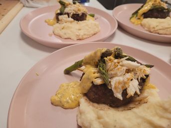 Gourmet beef patty topped with lump crab, asparagus and creamy hollandaise-style sauce served over mashed potatoes on a pink plate