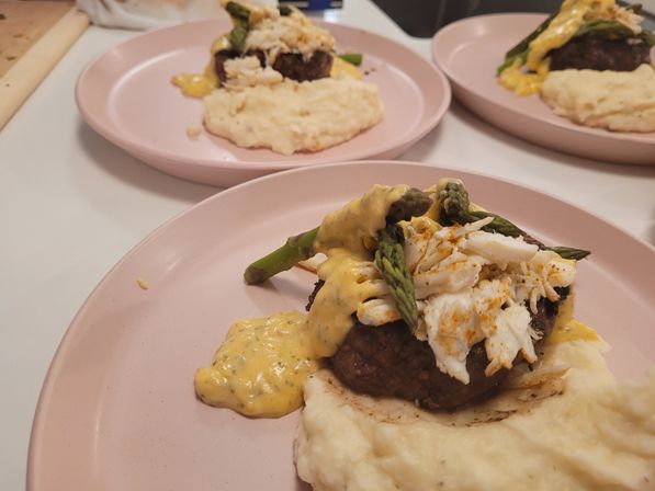 Three pastel-pink plates each with a crab-topped beef medallion, asparagus spears, creamy hollandaise and mashed potatoes — a gourmet surf-and-turf style dish.