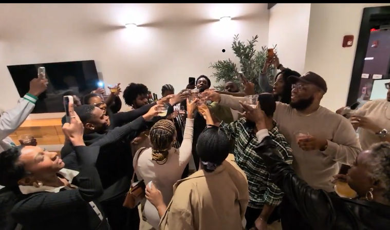 Lively indoor party with a diverse group raising glasses for a toast in a modern living room, many filming on smartphones.