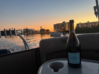 Bottle of prosecco on a boat table at sunset, waterfront condos and marina lights reflecting on calm bay water