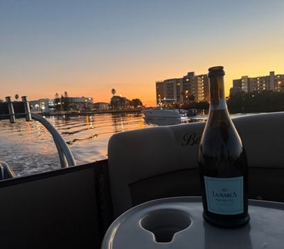 Bottle of prosecco on a boat table at sunset, waterfront condos and marina lights reflecting on calm bay water