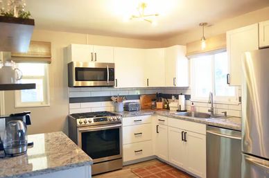 Bright modern U-shaped kitchen in suburban home with white cabinets, stainless steel appliances, gas range and microwave, granite countertops and subway tile backsplash