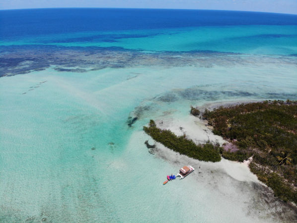 Aerial drone view of shallow turquoise tropical lagoon and sandbar with a small anchored boat and colorful inflatable slide beside a mangrove islet