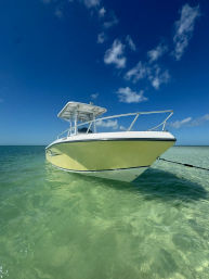 White center-console boat anchored in shallow crystal-clear turquoise water under a deep blue sky with scattered clouds — tropical coastal scene.
