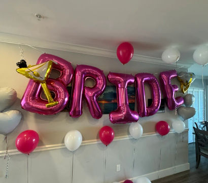 Pink metallic balloons spelling BRIDE with a gold martini-glass balloon and pink and white helium balloons decorating a home's dining area for a bachelorette/bridal shower