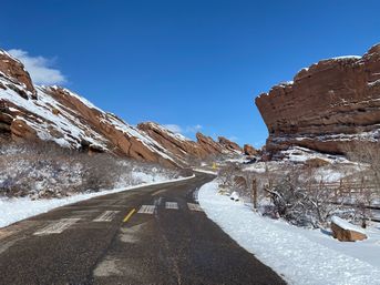 Winding empty road cutting through snow-dusted red sandstone cliffs beneath a vivid blue winter sky — a scenic red-rock winter drive.