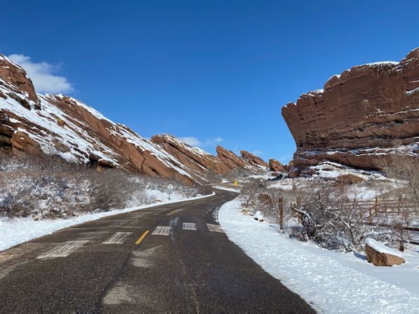 Winding empty road cutting through snow-dusted red sandstone cliffs beneath a vivid blue winter sky — a scenic red-rock winter drive.