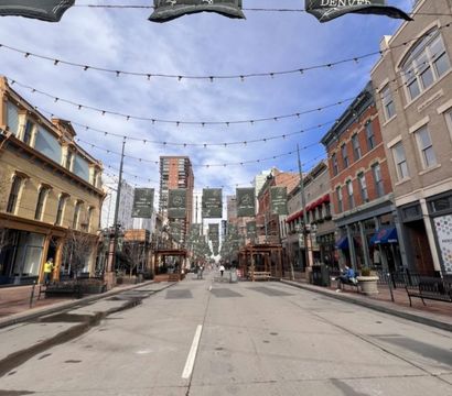 Cheerful downtown street scene with brick storefronts, overhead string lights and banners, outdoor seating and benches under a blue sky