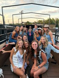 Group of smiling women in casual summer outfits on an open-air party bus trailer celebrating a bachelorette at sunset