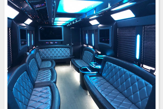 Luxury party bus interior with quilted leather bench seating, blue LED mood lighting, cupholder consoles and flat-screen entertainment