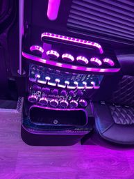 Luxury party-bus interior with purple LED ambient lighting, illuminated cup holders and shelves, quilted black leather seat and wood-look flooring