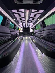 Luxury stretch limousine interior with black quilted leather bench seating, illuminated wood aisle and purple LED ceiling and accent lights for party transport