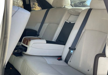 Beige leather rear seats in a luxury sedan with folded center armrest, wood-trim lid and pop-out cupholder, black seat belts and headrests.