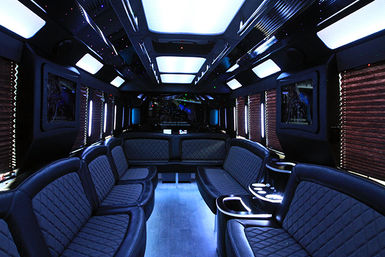 Luxury party bus interior with quilted black leather bench seats, blue LED ceiling and floor lighting, cup holders and flat-screen TVs for group nightlife transport