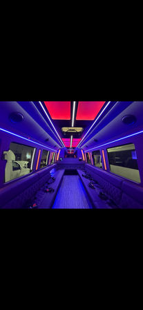 Vibrant party bus interior with purple and pink LED ceiling panels, quilted side bench seating, skylight window, and striped aisle floor.