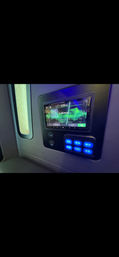 Passenger cabin wall-mounted touchscreen media display reading "No Bluetooth" with two USB ports and a panel of glowing blue lighting control buttons next to a small window — modern travel interior control panel.
