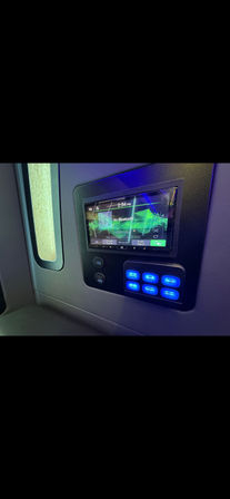 Passenger cabin wall-mounted touchscreen media display reading "No Bluetooth" with two USB ports and a panel of glowing blue lighting control buttons next to a small window — modern travel interior control panel.